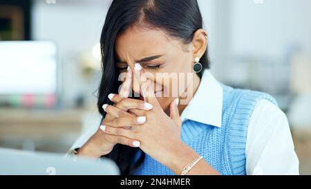 An overworked business woman with a headache while working in her office. A tired or stressed corporate female in pain at the workplace. A young Stock Photo