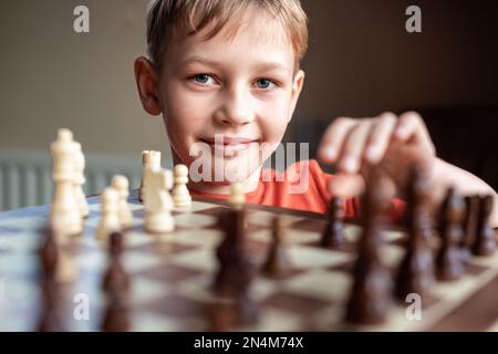 Young white child playing a game of chess on large chess board. Chess board on table in front of school boy thinking of next move, tournament Stock Photo