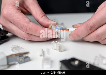 A woman's hand inserts an internet cable into a clamp connector. utp ethernet network cable plug. The concept of internet communications. Stock Photo