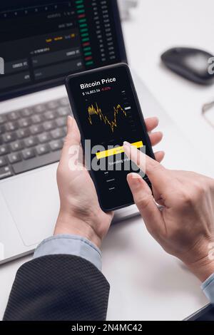 Broker or investor or cryptotrader using a smartphone application looks at financial data on the price of the stock market on a mobile phone, buys cry Stock Photo