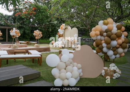 Creative gender neutral baby shower or birthday decoration in the garden. Bohemian style outdoor event set up with balloons. White cream peach caramel Stock Photo