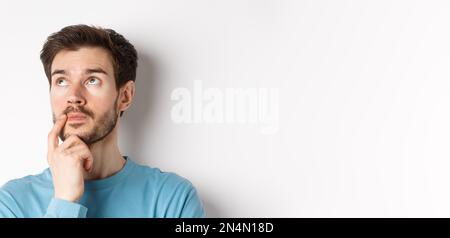 Face of young caucasian man looking up pensive, making choice or thinking, pondering while standing over white background Stock Photo