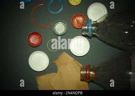 Plastic bottle caps, bottles and cardboard on a gray background. Concept of plastic waste problem and recycling. Stock Photo