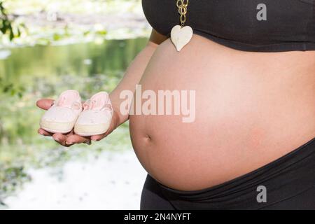 Pregnant woman belly, mother showing shoes for Her baby. Stock Photo