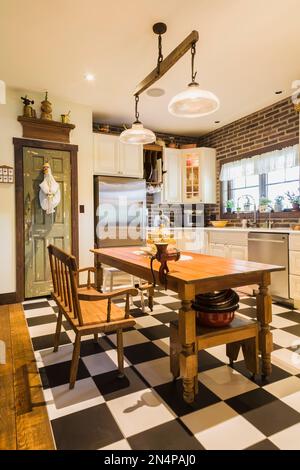 Kitchen with white cabinets, quartz countertops, antique wooden table and benches inside LEED certified country home. Stock Photo