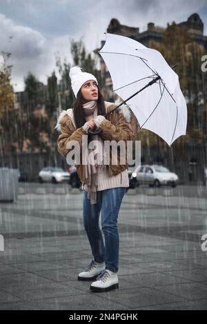 Woman with white umbrella caught in gust of wind on street Stock Photo