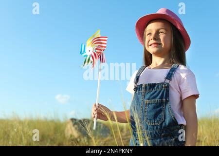 Cute little girl with pinwheel outdoors. Child spending time in nature Stock Photo