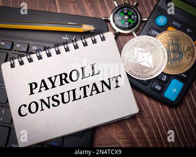 Notebook and digital coins with the word PAYROLL CONSULTANT on wooden background. Stock Photo
