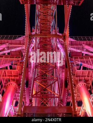 A bright red Ferris wheel attraction with a large metal construction glows creating a celebration in the dark with a light. Stock Photo