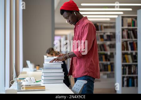 African American student guy standing in library looking for dissertation resources Stock Photo