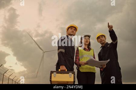 Three technician engineer in uniform with standing and checking wind turbine power farm power generator Station. Clean energy and environment. Stock Photo