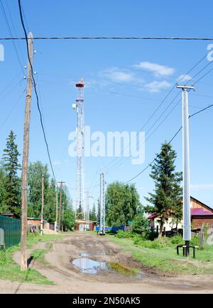 Power lines on concrete poles protected from impact by a car from below stand on a village street next to a puddle in the Northern Yakut village Stock Photo