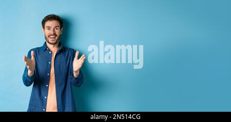 Cheerful young man pointing hands at camera and smiling, feeling glad for you, praising nice work, standing on blue background Stock Photo