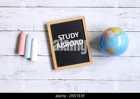 Top view of globe of world map,chalk and blackboard written with ' STUDY ABROAD' on white wooden background. Stock Photo