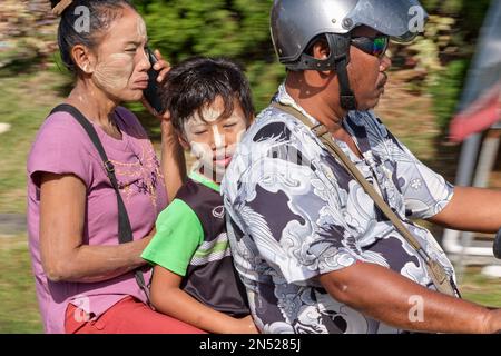 Members of a Myanmarese (Burmese) migrant family, father, mother and son, riding on a motorcycle in Phuket, Thailand, the mother talking on her mobile Stock Photo