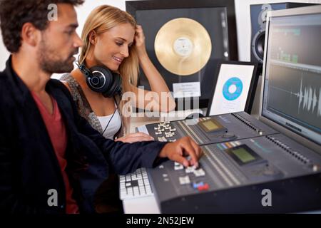 High resolution recording. A young audio engineer working on a mixing desk with his blonde colleague sitting next to him. Stock Photo