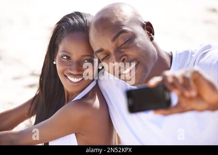 Smile for me...A happy young african couple smiling while taking a snapshot on the beach. Stock Photo