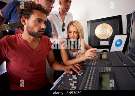 Getting the balance just right. Four young music producers working on a mixing desk in their studio. Stock Photo