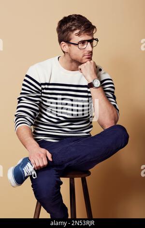 Hes a thinking man...Studio shot of a thoughtful-looking young man sitting on a stool. Stock Photo