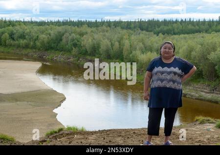 Full Yakut Asian girl stands on the edge of a cliff on the background of taiga forest and river in the North of Yakutia. Stock Photo