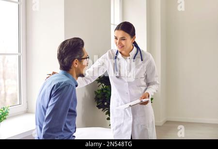 Professional female doctor approvingly, carefully puts her hand on the shoulder of young male patient. Stock Photo