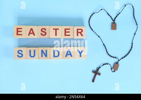 Easter Sunday holy week concept. Wooden blocks typography with rosary flat lay in blue background. Stock Photo