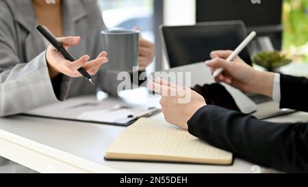 Two businesswomen are discussing, sharing ideas on a new project, working together in the office. A businesswoman sipping coffee while talking with he Stock Photo