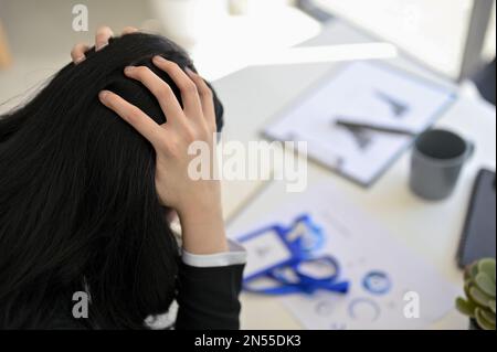 Stressed and furious Asian businesswoman or female office worker sits at her office desk, suffering from hard working. close-up back view image Stock Photo
