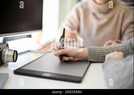 Professional and creative female graphic designer designing her artwork on computer, using graphic tablet and stylus pen, working with her colleague i Stock Photo