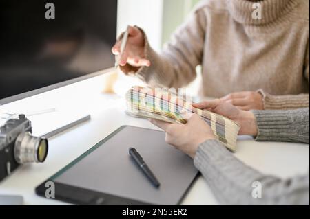 Close-up image of two professional and creative female graphic designers working together in the office, choosing colors on color chart. Stock Photo