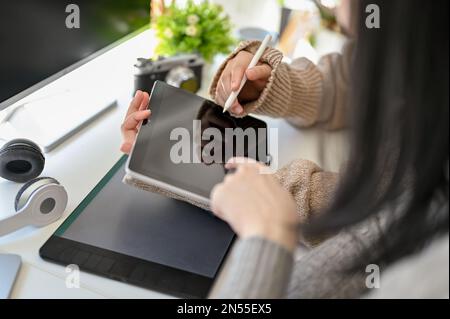 Cropped image, Two Asian female graphic designers looking at something on a tablet screen, discussing and working together in the office. Stock Photo