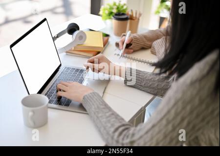 Two professional Asian female office workers remote working at co-working space together, discussing and planning project, using laptop. laptop white Stock Photo