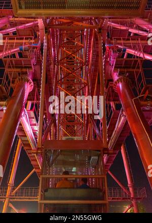Bright red attraction glowing Ferris Wheel with a large metal structure and a cabin with the backs of people working at night in Novosibirsk. Stock Photo