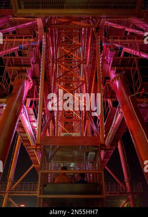 Bright red attraction glowing Ferris Wheel with a large metal structure and a cabin with the backs of people working at night in Novosibirsk. Stock Photo
