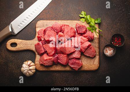 https://l450v.alamy.com/450v/2n56dfb/raw-beef-meat-chopped-in-cubes-with-bunch-of-fresh-parsley-garlic-salt-and-pepper-on-wooden-cutting-board-with-knife-for-cooking-stew-or-meat-dish-2n56dfb.jpg