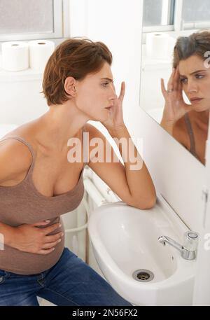 Not feeling it today. a pregnant woman holding her stomach in discomfort in the bathroom. Stock Photo