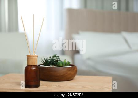Air reed freshener and houseplants on wooden table in bedroom. Space for text Stock Photo