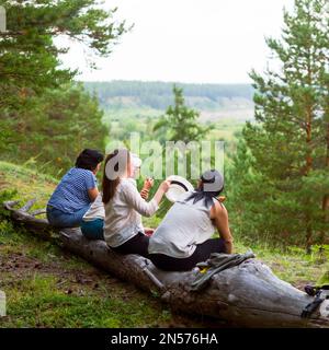 Four girls Yakut friends sitting on a log and communicate against the background of the wild North of the taiga and streams. Stock Photo