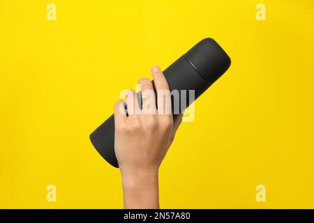 Woman holding modern black thermos on yellow background, closeup Stock Photo