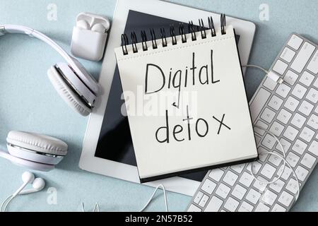 Flat lay composition of notebook with words DIGITAL DETOX and different gadgets on light blue background Stock Photo
