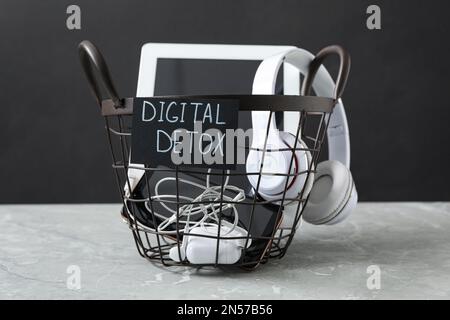 Trash bin with different gadgets and words DIGITAL DETOX on light grey marble table Stock Photo