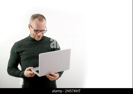 Focused man in glasses using a laptop, typing on the keyboard, writing an email or message, chatting, shopping, a successful freelancer working online on a computer stands on a white background Stock Photo