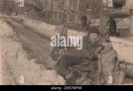 Vintage photograph about a super winter time when we had have fun togedher. We were sledging in the snow at the road. Our big German Sheperd dog was pushing us to get moved. Our little puppy was too small to get help him, but he could manage it. that time was 1930s. Stock Photo