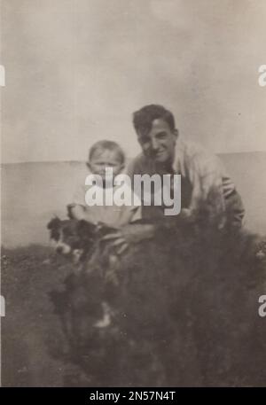 Vintage Photograph about pet dogs  /hand holding puppy. Little boy standing with his little black dog at his father outside at the 1930s. Happy moment visible in the photo. Father is super happy and proud of his son. Stock Photo