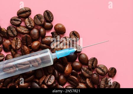 Syringe with coffee beens on pink background - Concept of coffee and health Stock Photo