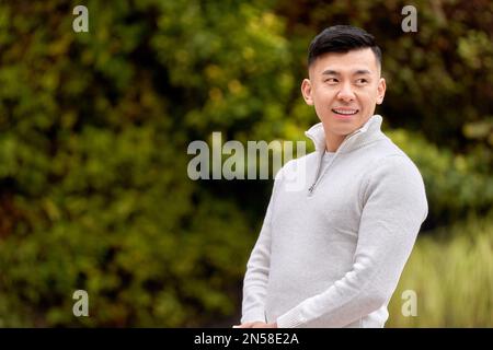 Attractive Asian man looking to the side smiling while relaxing outdoors in a park.  Stock Photo