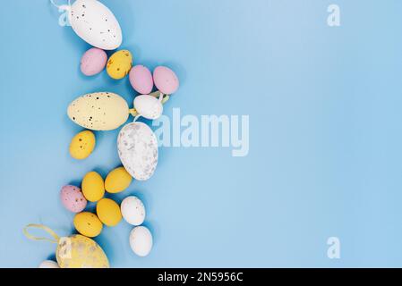 Easter card. Multi Colored Easter eggs of different sizes and colors - pink, yellow, white on a blue background. Copy space for text. Flat Lay Stock Photo