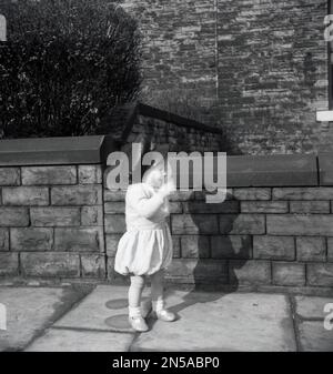 1950s, historical, summertime and an excited infant child outside on a pavement, wearing a postman's cap, England, UK. Stock Photo