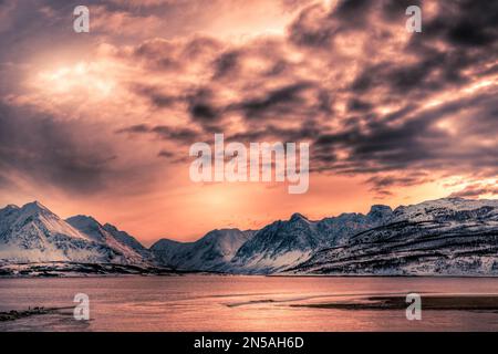 An amazing sunset taken across a lake looking towards snowy mountains near Tromso in the far North of Norway Stock Photo
