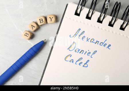 Notebook with different baby names, pen and wooden cubes on grey marble table, flat lay Stock Photo